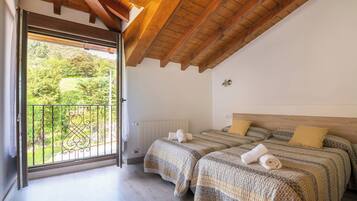 Un dormitorio con dos camas, techo de madera, vista a follaje exterior y balcón con barandilla metálica.