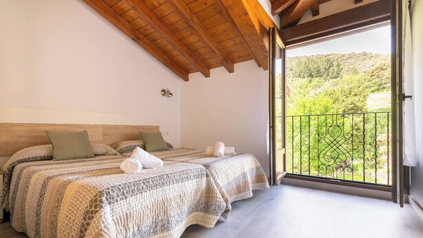 A bedroom with two beds, a wooden ceiling, and a balcony with a view of greenery. - Tranquillity by Fidalsa (Cabezón de Liébana)