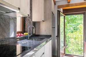 A modern kitchen with a black marble countertop, stainless steel sink, and a view of greenery through a sliding glass door.