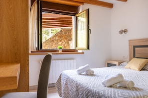 A bedroom with a bed, a window with curtains, a small plant, and a wooden headboard.