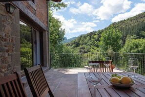 Une terrasse avec un sol en pierre, des meubles en bois et une vue sur une colline boisée.