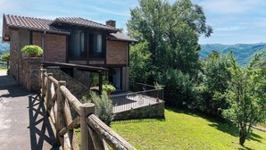 Uma casa de dois andares com fachada de pedra, uma varanda e vista para a paisagem ao redor.