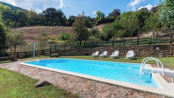 Una piscina con borde de piedra, rodeada por un muro de piedra y una valla de madera.