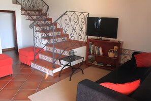 Ein Wohnzimmer mit Treppe, Fernseher, Bücherregal und Sofa.