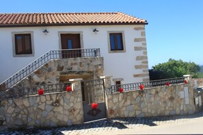A two-story building with a stone facade, a tiled roof, and a metal staircase with red decorations.