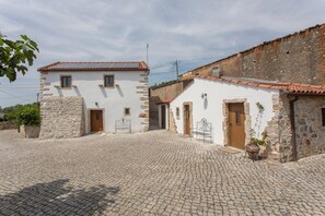 A traditional stone building with a tiled roof, a cobblestone courtyard, and a small garden area with a potted plant.