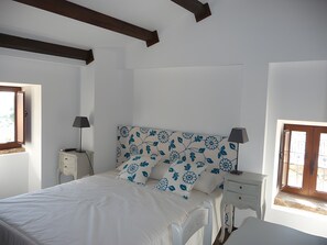 A bedroom with a bed, two bedside tables, a window, and a wooden ceiling beam.