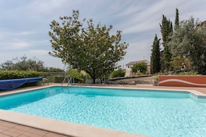 A swimming pool with a slide, surrounded by trees and a stone wall.