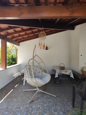 A covered patio area with a hanging chair, a table with a basket, and a hanging dreamcatcher. - Casa Mãe: Holiday Home with Mountain View, Wi-Fi and Air Conditioning (Pousadas Vedras)