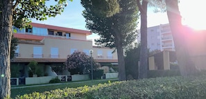A multi-story building with balconies, a garden area, and a tree in the foreground. - ✨La Romantique Villa (Le Grau du Roi)
