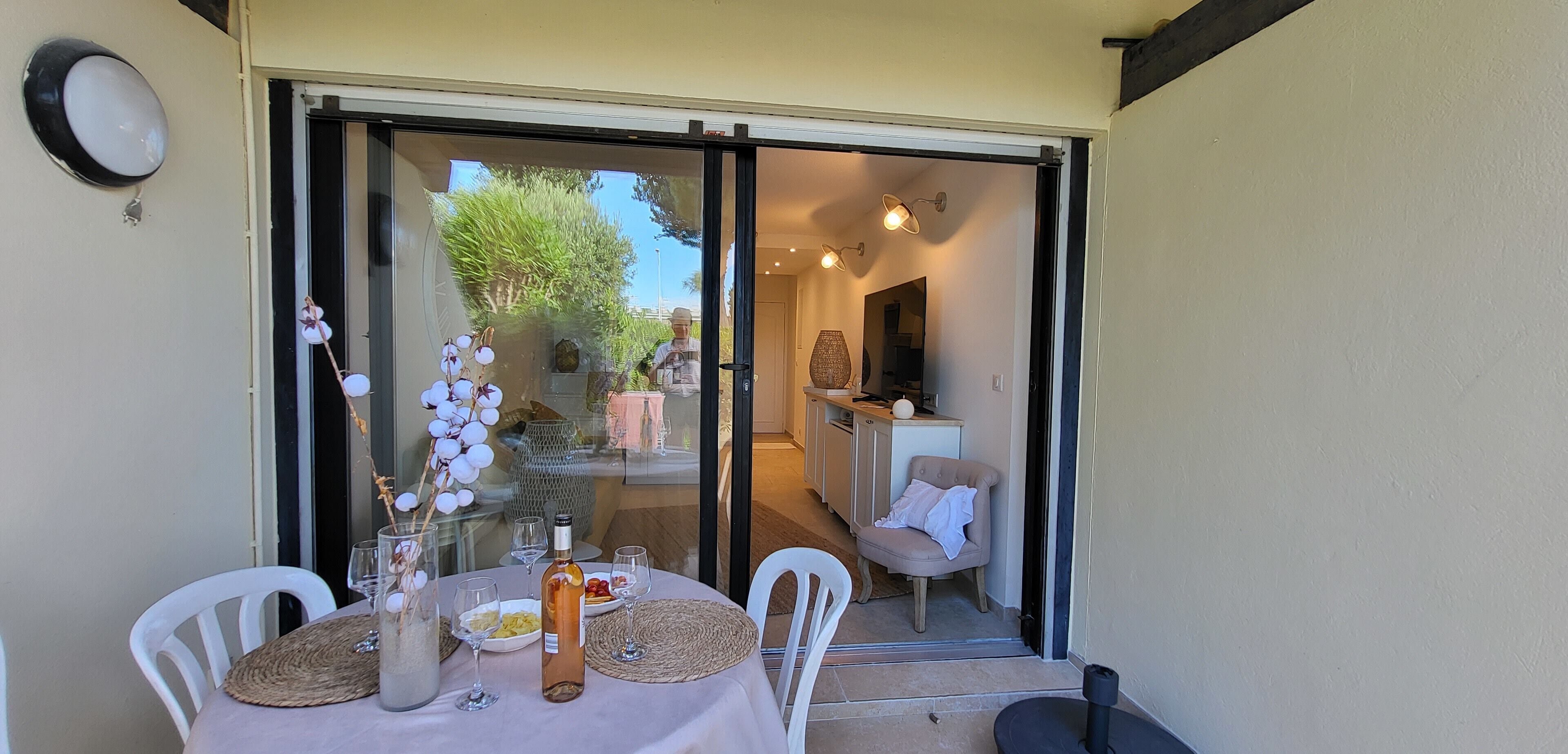 A dining area with a table set for two, a bottle of wine, and a vase of flowers.
