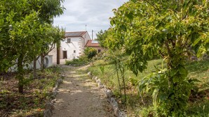 Ein ländlicher Pfad führt zu einem Steinhaus mit Ziegeldach, umgeben von üppigem Grün und Bäumen.