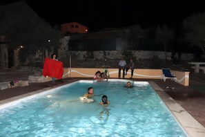 Une piscine entourée de personnes, un mur de pierre et un bâtiment en arrière-plan.