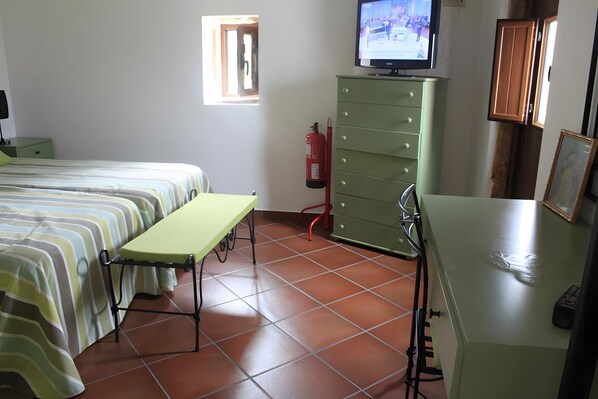 Une chambre avec deux lits, un bureau, une télévision, une armoire verte et un extincteur.