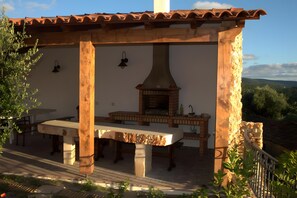 Un patio al aire libre con horno de ladrillo, mesa de madera y bancos.