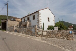 Un edificio blanco con paredes de piedra y techo de tejas, una escalera de piedra y una calle pavimentada al frente.