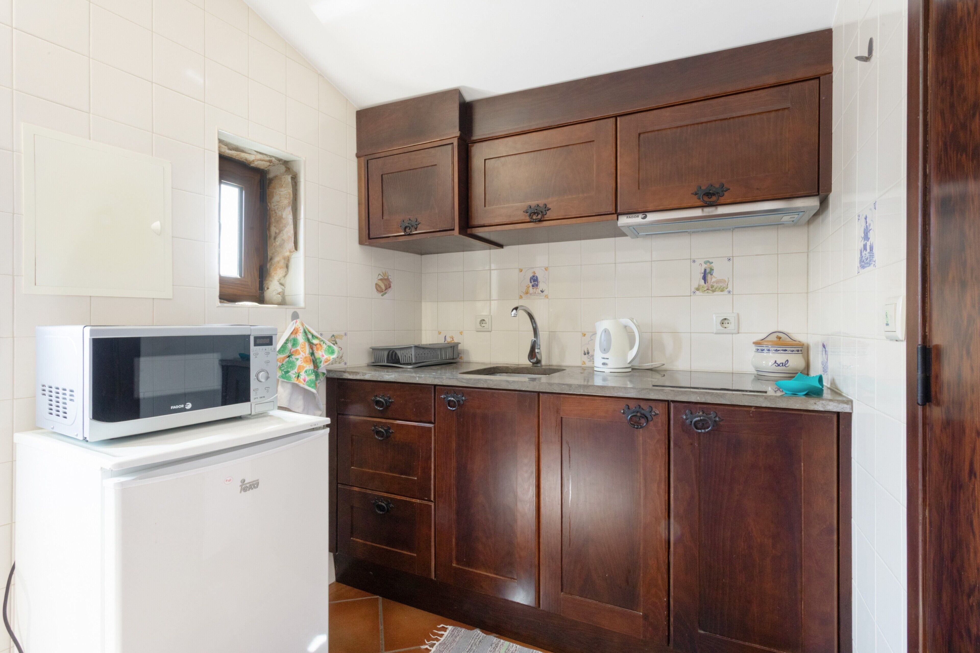 Una cocina con armarios de madera, microondas, hervidor y fregadero.