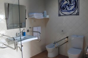 Une salle de bain avec une douche à parois de verre, un lavabo blanc muni d’une barre d’appui, un bidet et des toilettes.