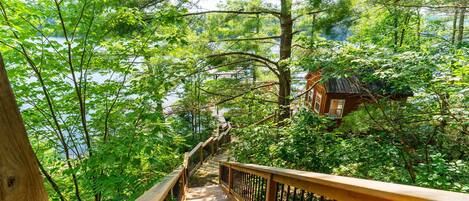Una escalera de madera que serpentea por un bosque, con vistas a un lago y un edificio pequeño en la distancia.