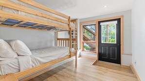 A bunk bed room with a wooden floor, a black door, and a window with a view of greenery.