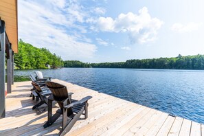A wooden dock with chairs, a lake, and a forested shoreline.