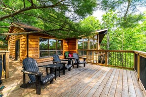 A wooden cabin with a deck, outdoor seating, and a large window overlooking the forest. - Lake It Easy | On Portage Lake (Parry Sound District)