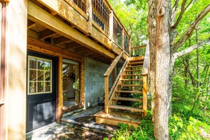 A wooden cabin with a staircase leading to a deck, surrounded by trees.