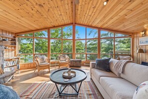 A spacious room with large windows, a round coffee table, a sofa, and a fireplace. - Lake It Easy | On Portage Lake (Parry Sound District)