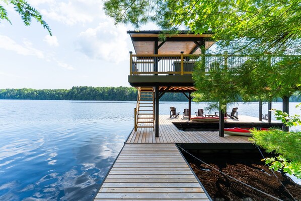 Une terrasse en bois menant à un chalet offrant une vue sur un lac et une forêt.