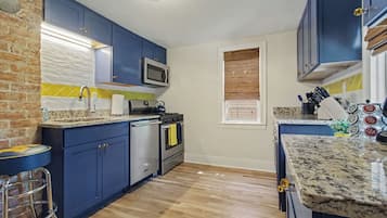 A kitchen with blue cabinets, a stainless steel stove, a microwave, and a wooden floor.