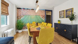 En spiseplads med et muralmaleri af et fodboldstadion, gule stole, et træbord og et mørkt skab med geometriske mønstre.