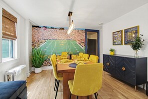Un coin repas agrémenté d’une fresque représentant un stade de football, de chaises jaunes, d’une table en bois et d’un buffet sombre orné de motifs géométriques.