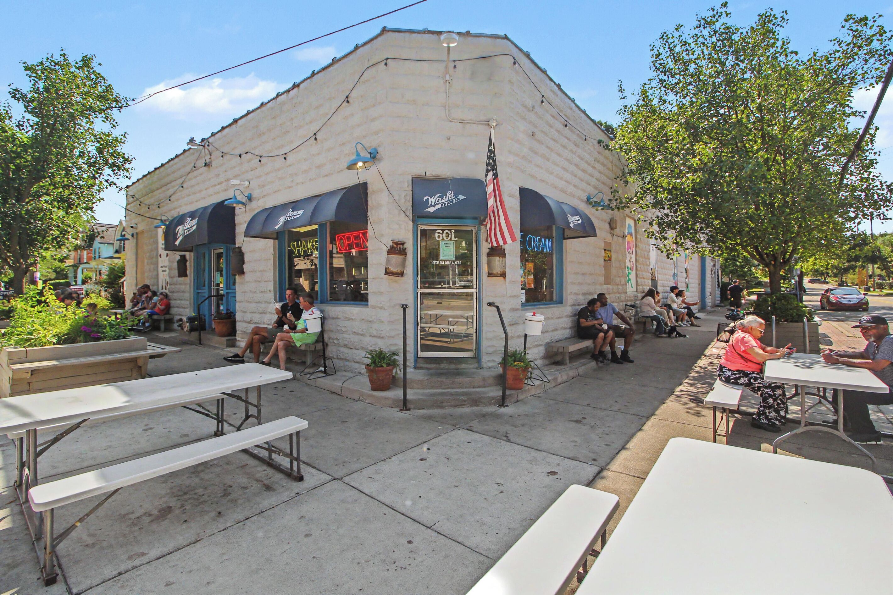 A small, single-story building with a flat roof, a storefront with a neon sign, and outdoor seating with tables and benches.