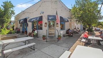 A small, single-story building with a flat roof, a storefront with a neon sign, and outdoor seating with tables and benches.