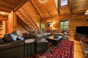Ein Holzblockhaus-Interieur mit einem Ecksofa, einem Couchtisch, einem Fernseher und einer Treppe.
