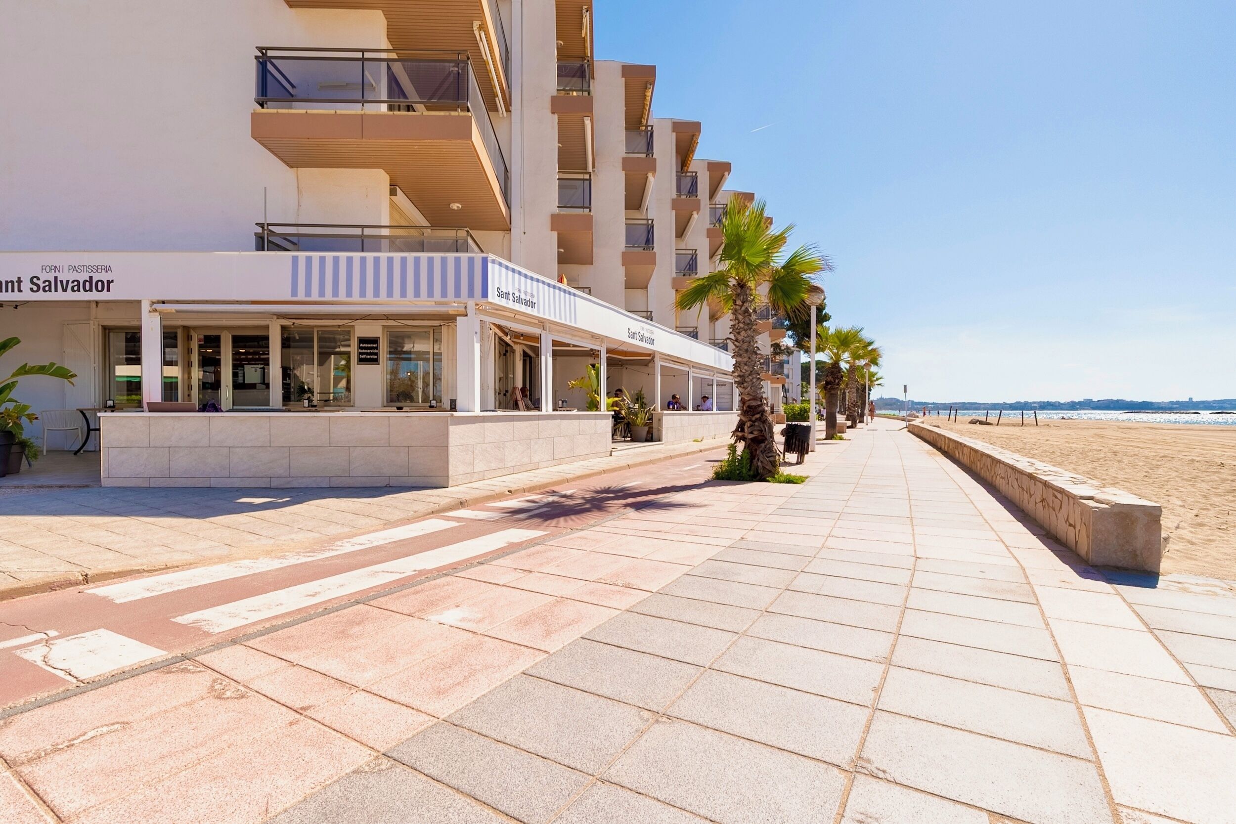 A beachfront hotel with a covered walkway, palm trees, and a clear view of the ocean.