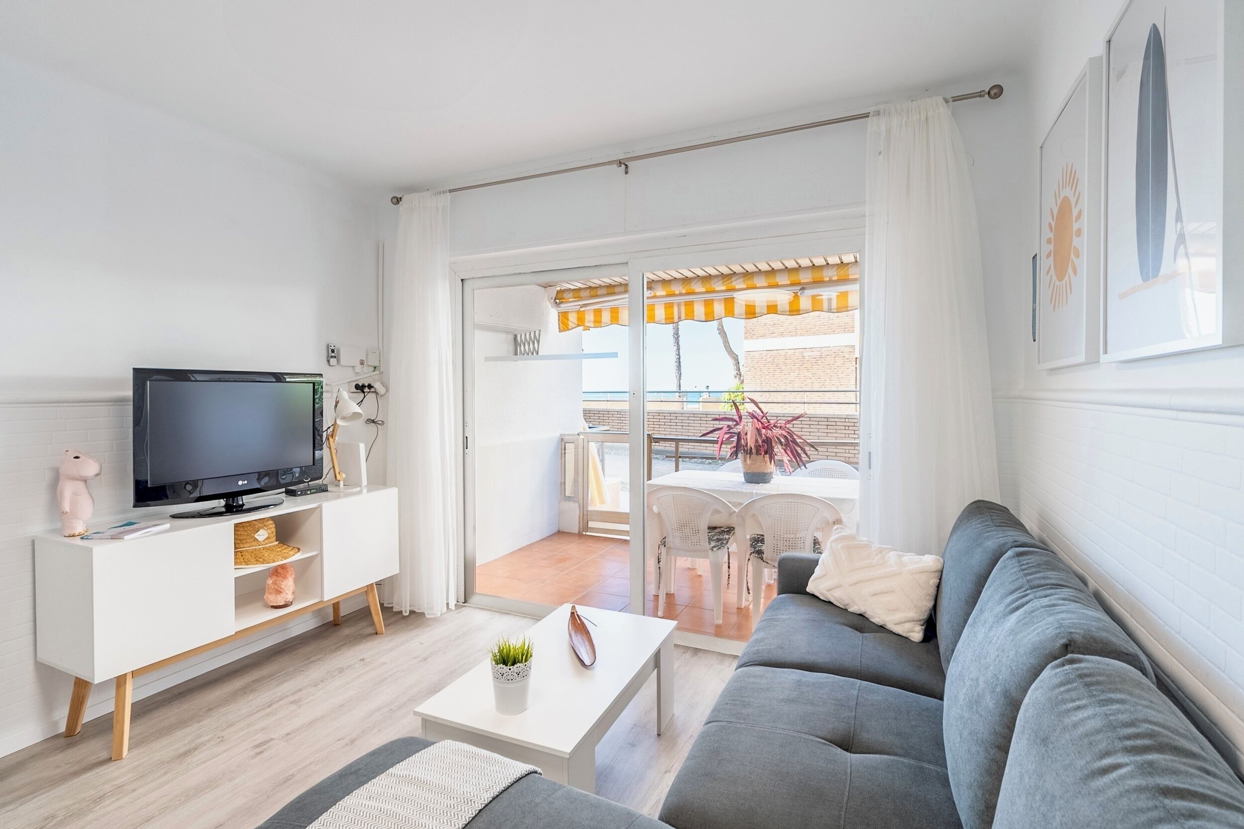 A modern living room with a grey sofa, white TV stand, and a balcony with outdoor furniture.