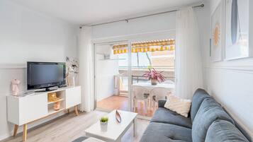 A modern living room with a grey sofa, white TV stand, and a balcony with outdoor furniture.