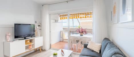A modern living room with a grey sofa, white TV stand, and a balcony with outdoor furniture.