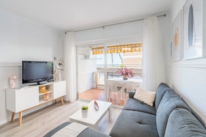 A modern living room with a grey sofa, white TV stand, and a balcony with outdoor furniture. - Beachfront Apartment with Terrace & Ocean Views (Cambrils)