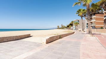 A beachside promenade with a clear view of the sea, palm trees, and a row of buildings.