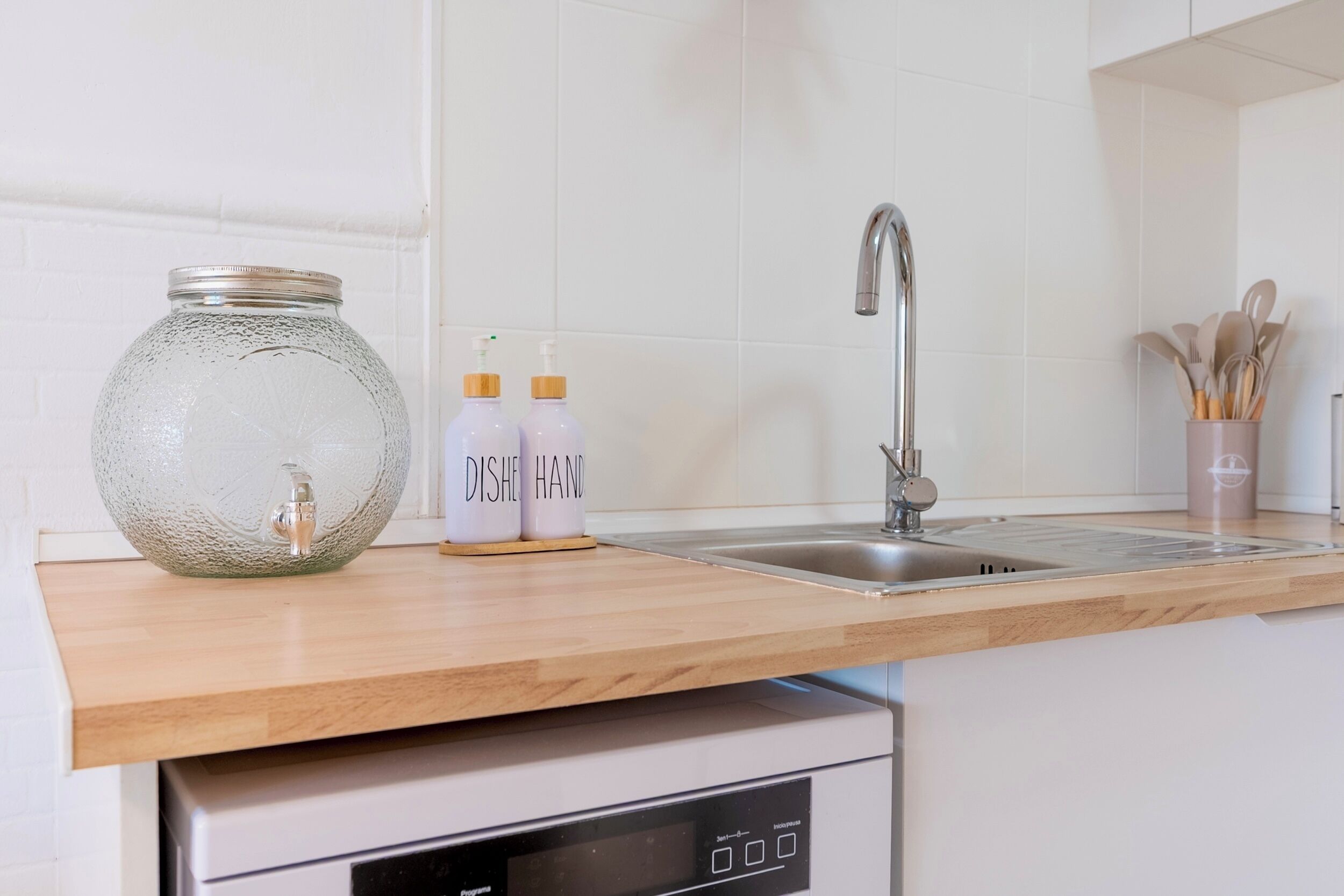Une cuisine équipée d’un évier en acier inoxydable, d’un lave-vaisselle et d’un plan de travail en bois.