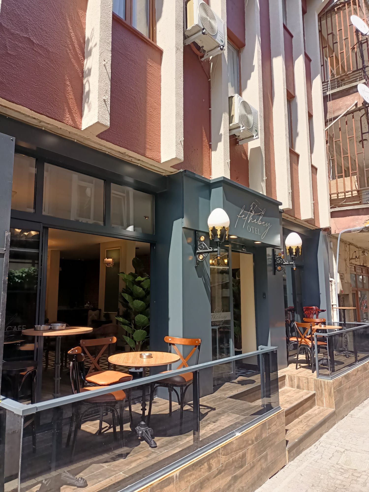 An outdoor seating area with tables and chairs, a sign for 'feThibey OTEL', and a staircase leading to the entrance.