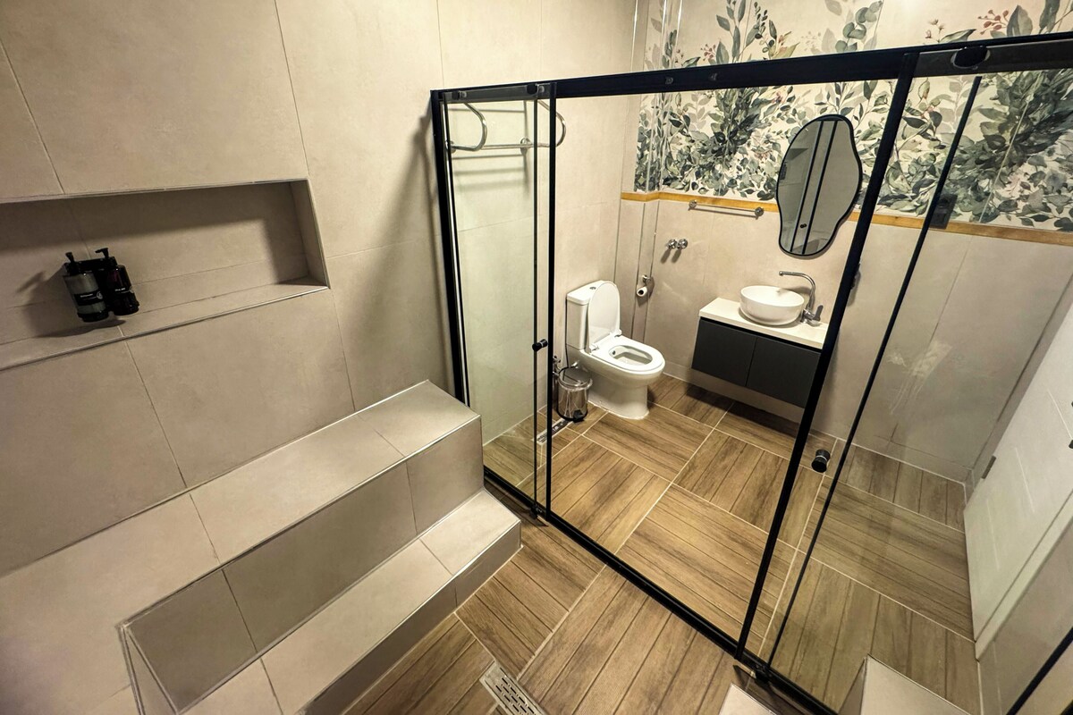 Een moderne badkamer met een douchecabine van glas, een toilet, een wastafel en een spiegel.