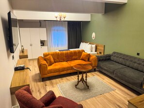 Een moderne woonkamer met een bank, een rode fauteuil, een salontafel en een aan de muur bevestigde televisie.