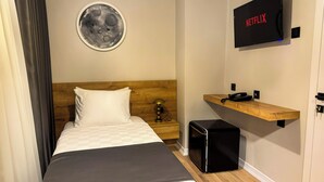 A hotel room with a bed, a small bedside table, a wall-mounted TV, a wooden shelf, and a wall clock. - Fethibey Otel (Bartın)