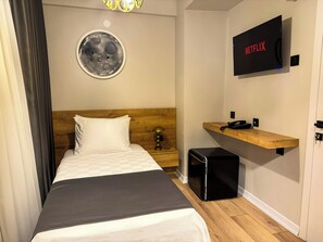 Een hotelkamer met een bed, een klein nachtkastje, een wandtelevisie, een houten plank en een wandklok.