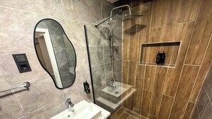 A modern bathroom with a vanity, a mirror, a shower, and a small shelf. - Fethibey Otel (Bartın)