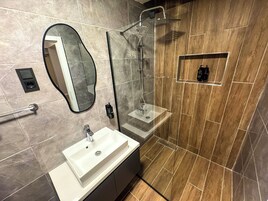 Un baño moderno con tocador, espejo, ducha y un estante pequeño.