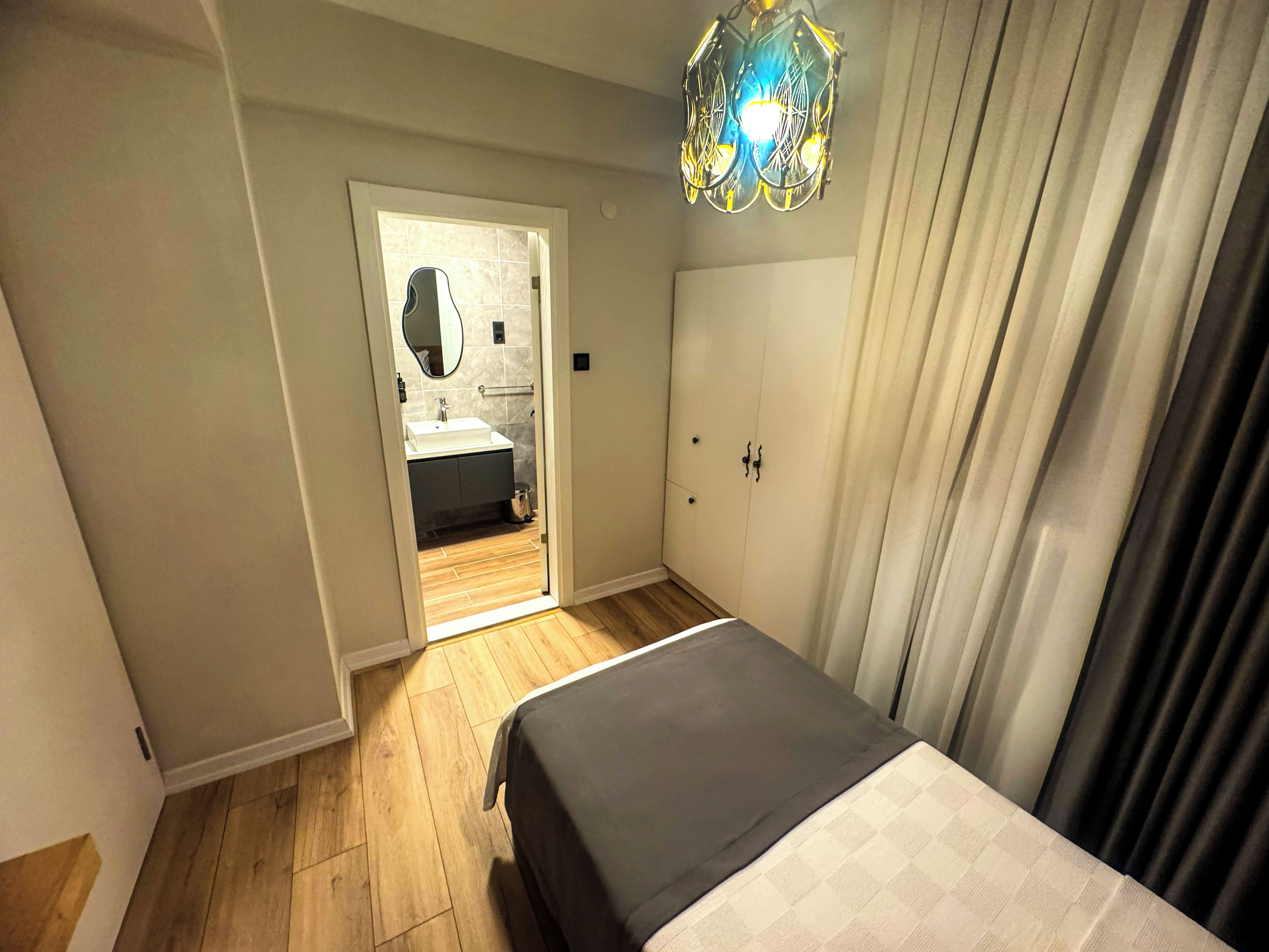 A bedroom with a bed, a wardrobe, a bathroom with a mirror, and a hanging light fixture.